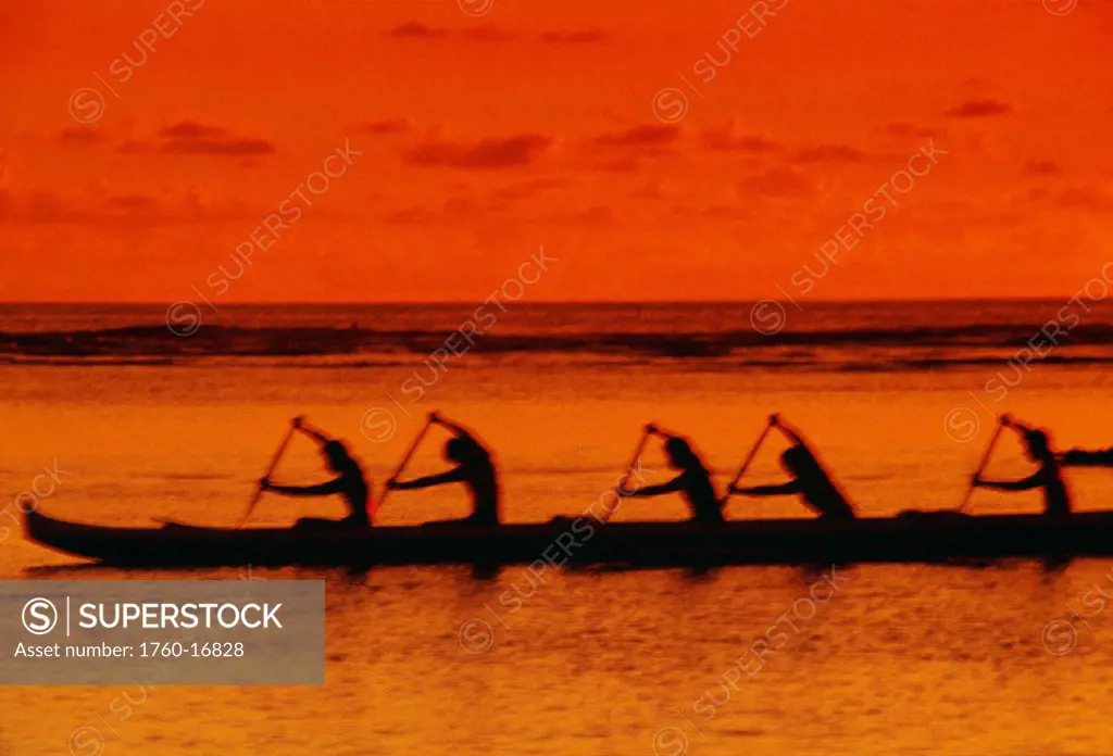 Side view of paddlers in an outrigger at sunset, arms raised, golden orange hue.