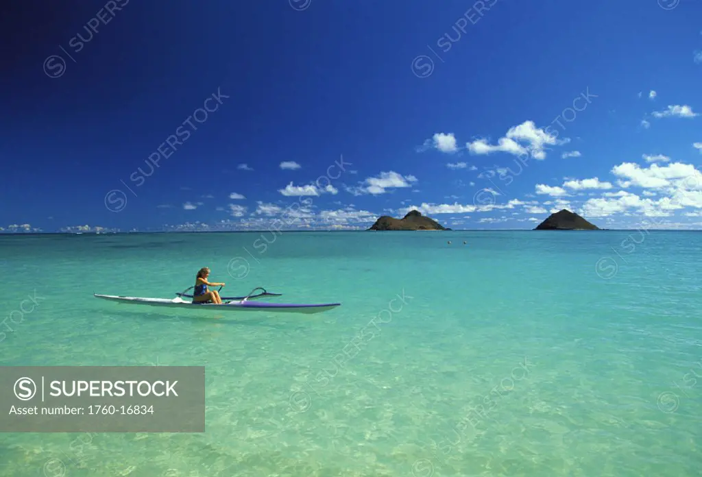 Hawaii, Oahu, Side view of woman in distance paddling single outrigger, turquoise water, Mokulua Islands in background
