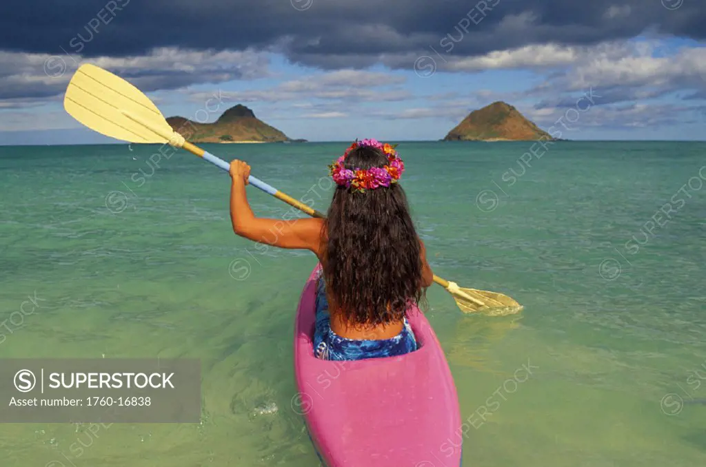Back view of woman in kayak, yellow paddles, pink lei, clear water, blue sky