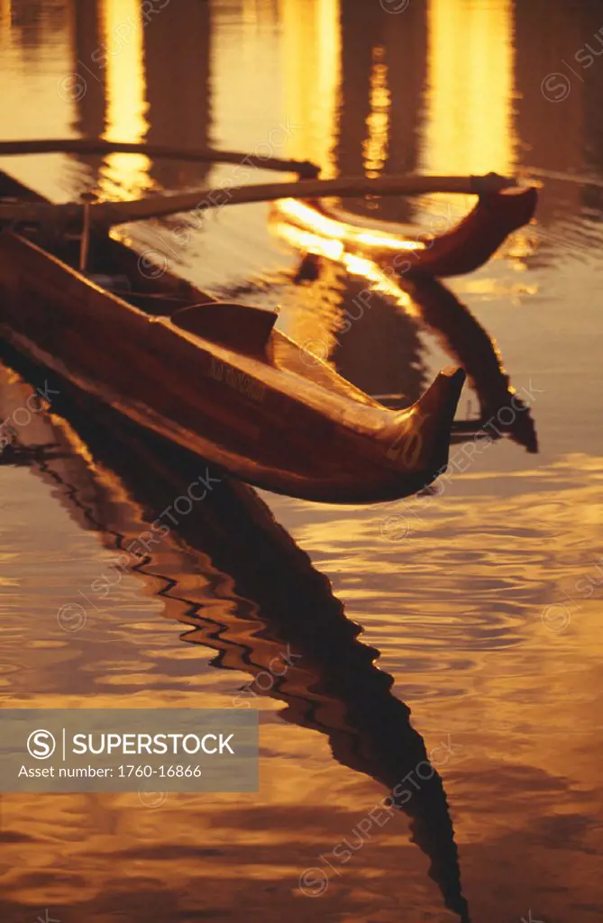 Closeup of koa outrigger canoe on water with reflection of golden sunset.