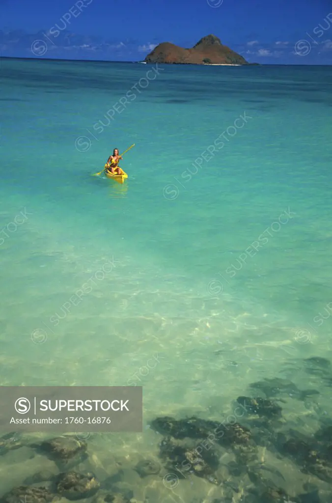 Hawaii, Oahu, Lanikai, Woman kayaking in turquoise ocean Mokulua Islands background, blue sky