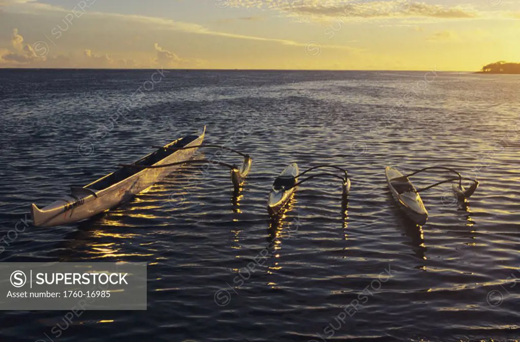 Hawaii, Three outrigger canoes float on rippling ocean water at sunset.
