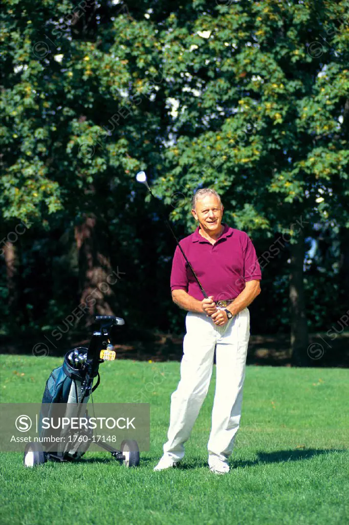 Smiling senior man with golf club in hand, next to bag of clubs C1271