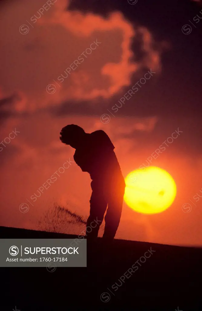 Silhouetted golfer @ sunset, in sand trap, sunball behind dramatic orange sky