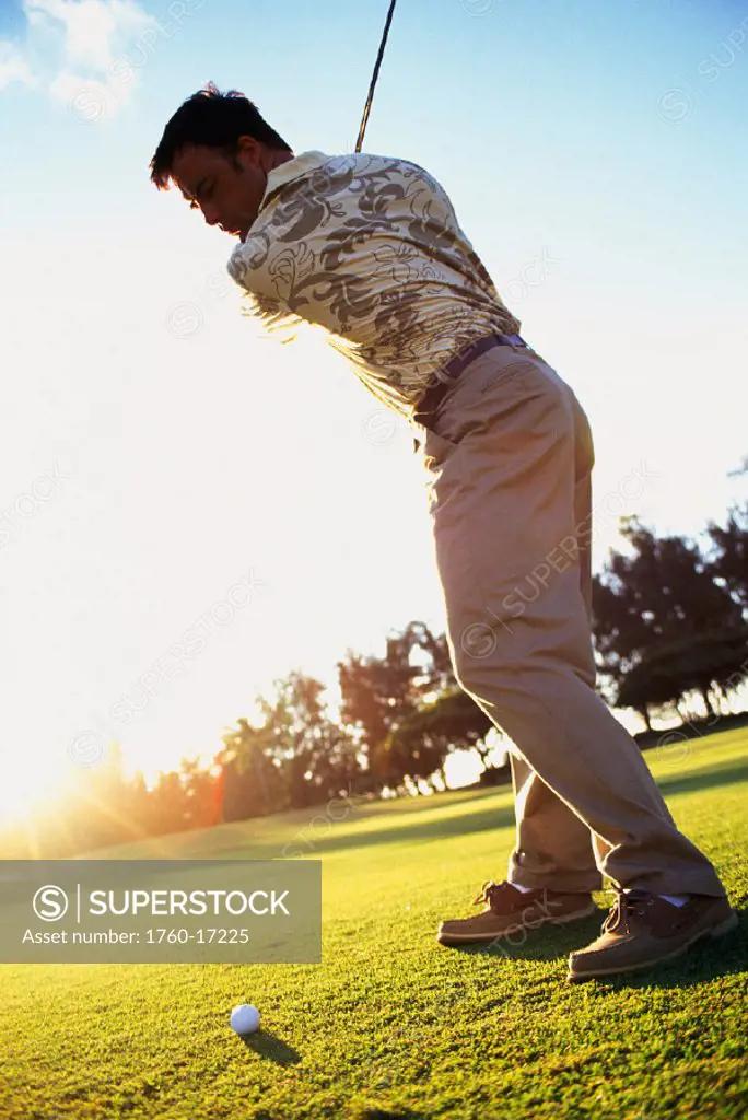 Hawaii, Golfer in mid-swing. Sunburst light in background.