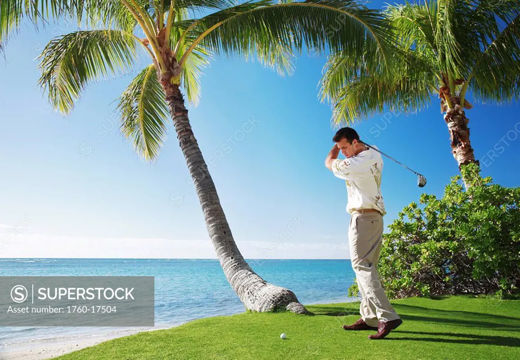 Hawaii, Oahu, Male playing golf, ready to swing his golf club at a beach front golf course