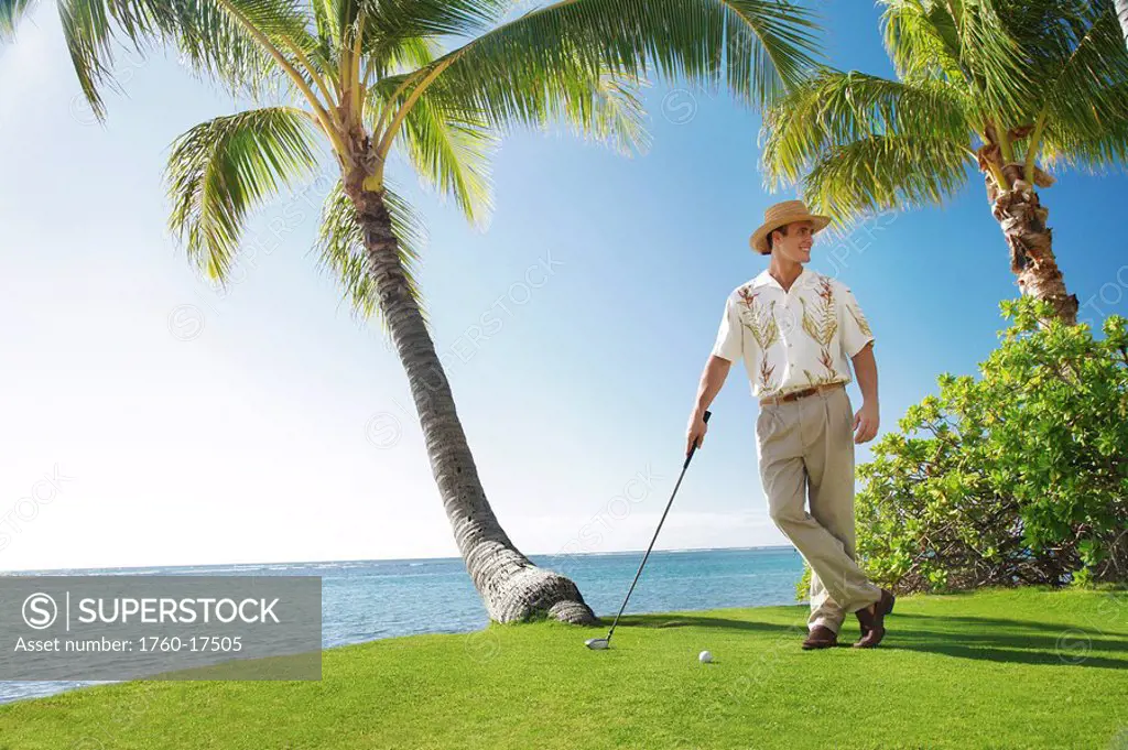 Hawaii, Oahu, Caucasion Male standing and posing with a Golf Club and Golf ball in hand at a beautiful tropical beachfront golf course turf