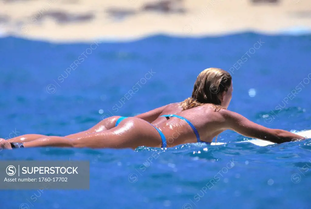 Woman surfer paddling to shore, view from behind, thong