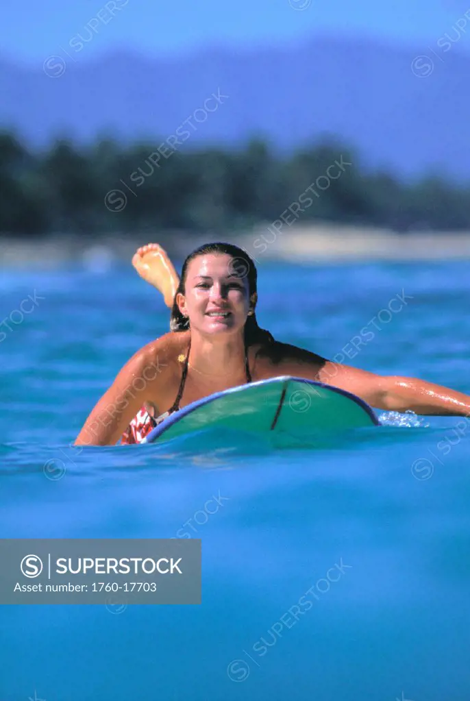 Front view of woman on surfboard paddling out, smiling