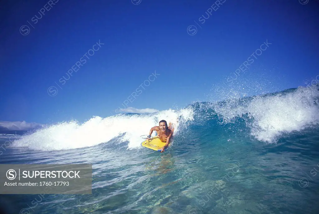 Front view woman riding shorebreak wave, smiling cloudless blue sky D1217 bodyboarder
