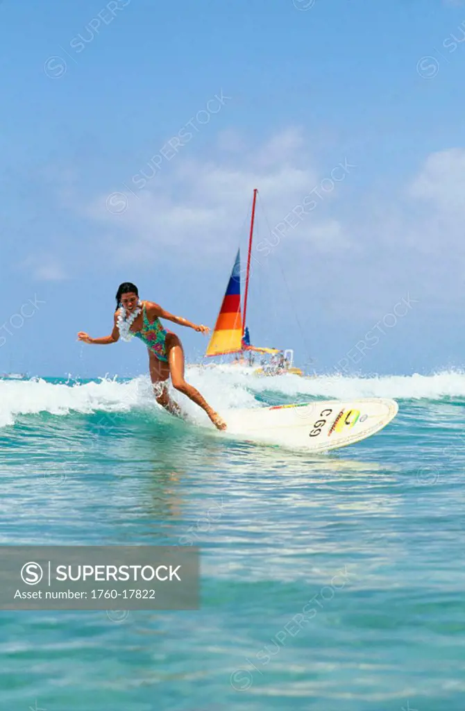 Hawaii, Beautiful young woman surfing wave, wearing lei