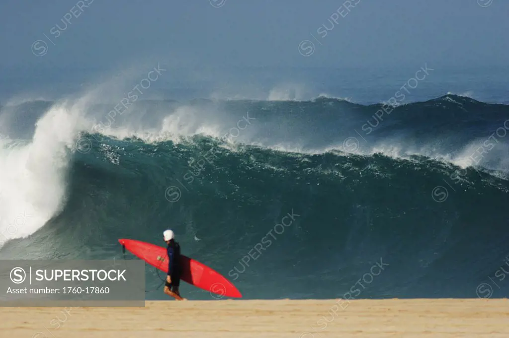 Hawaii, Oahu, Waimea Bay, Surfer walking on beach wearing helmet, big shorebreak