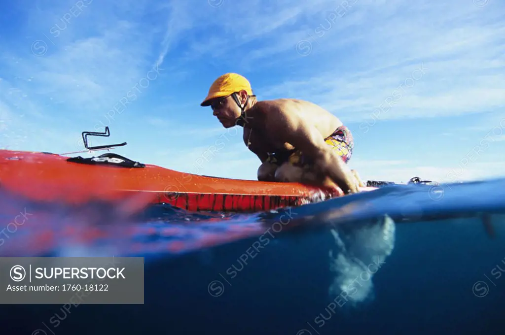 Hawaii, Over/Under view of man paddleboarding, leaning forward on red board.