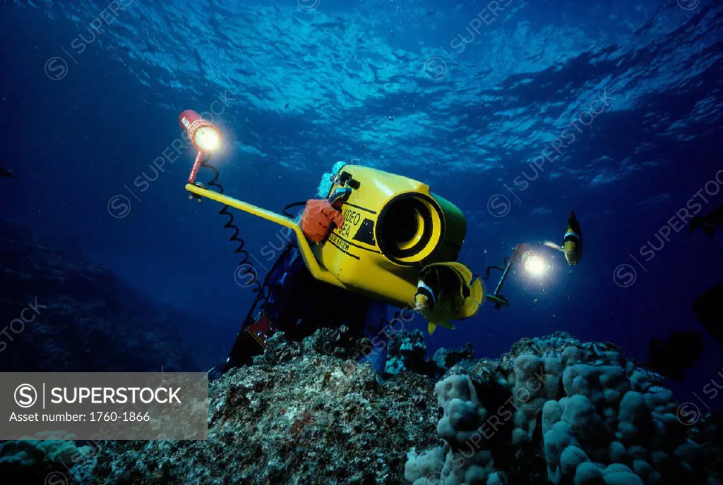 Hawaii, diver w/ underwater video camera over coral reef surface visible A80A
