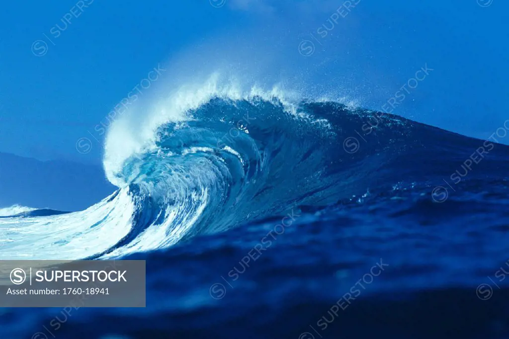 Side angled view of big blue wave curling with spray, blue skies in bkgd GR6735