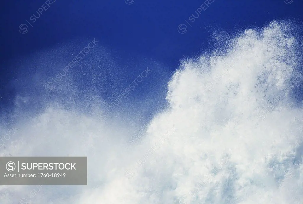 Closeup of white wash from huge crashing wave in blue sky.