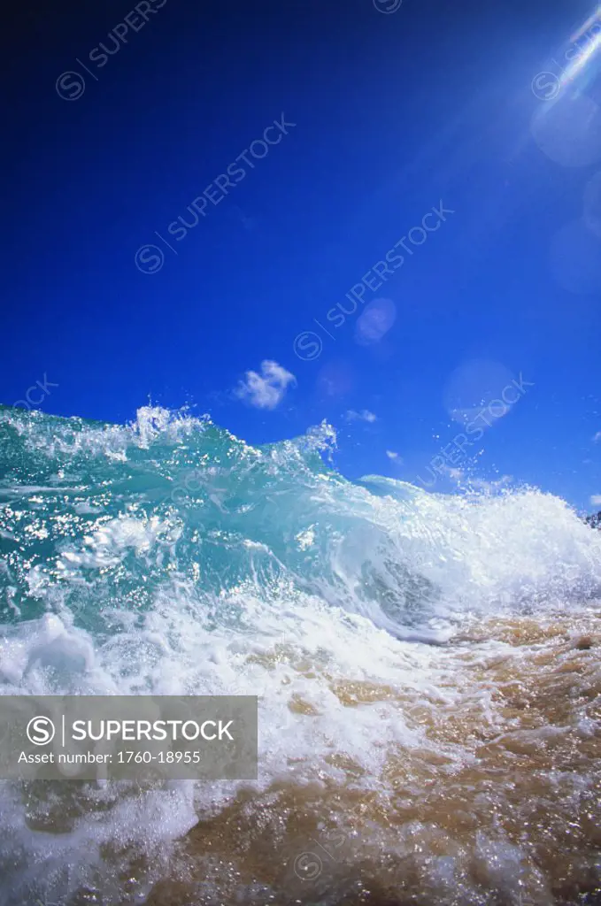 Turbulent shoreline break water, sun rays in clear blue sky.