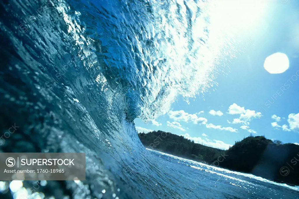 Translucent curling blue wave backlit, shimmery waters, land in bkgd