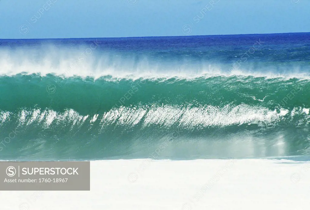Shimmery shorebreak wave with silver waters in foreground.
