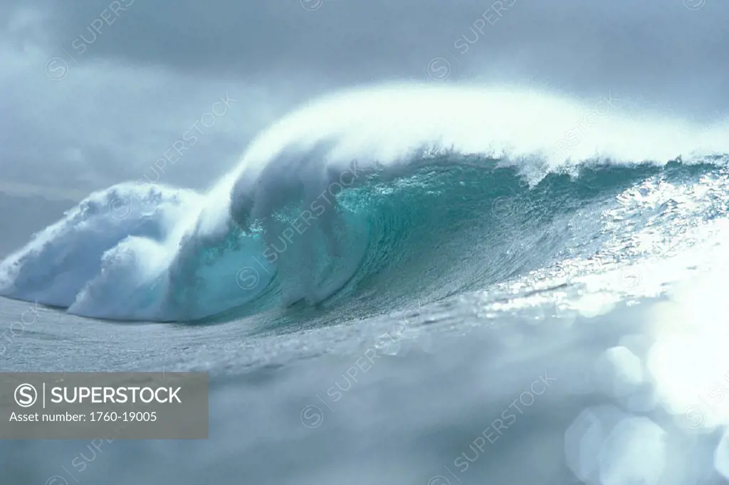 Large wave with spray breaks toward shoreline, silver shimmery ocean