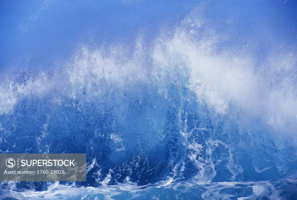 Blue waves crashing on the shore with blue sky background