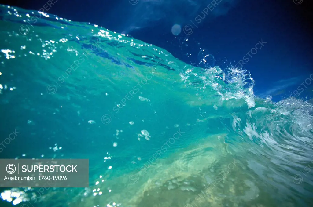 Hawaii, Turquoise breaking wave, sand visible through clear water, blue sky. Close-up.