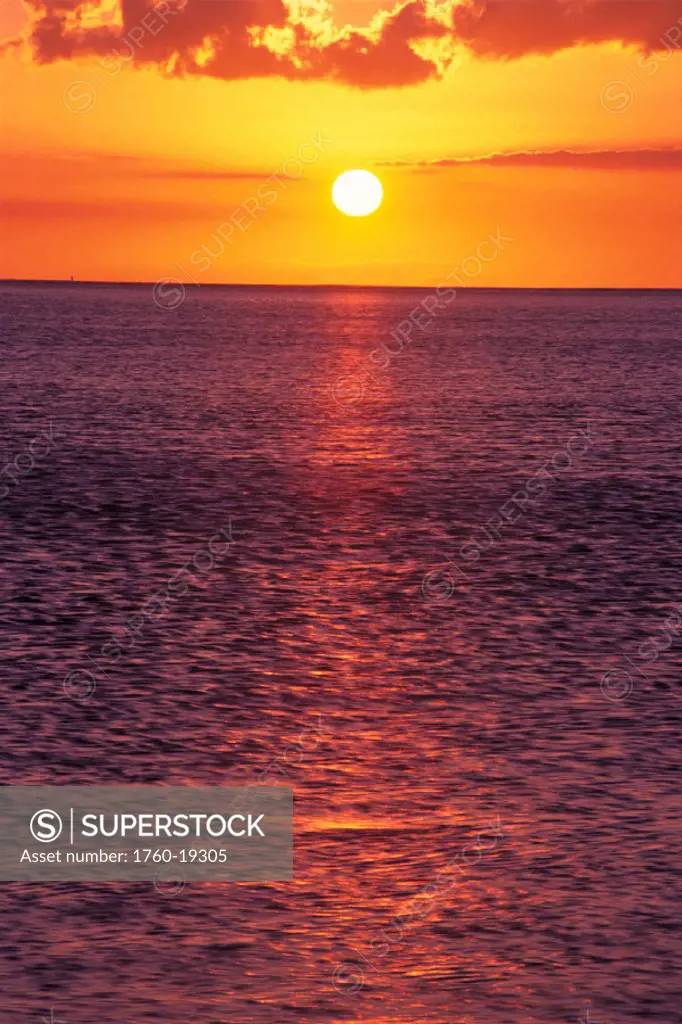 Golden sunball, sunset with orange sky over ocean purple surface w/ reflections