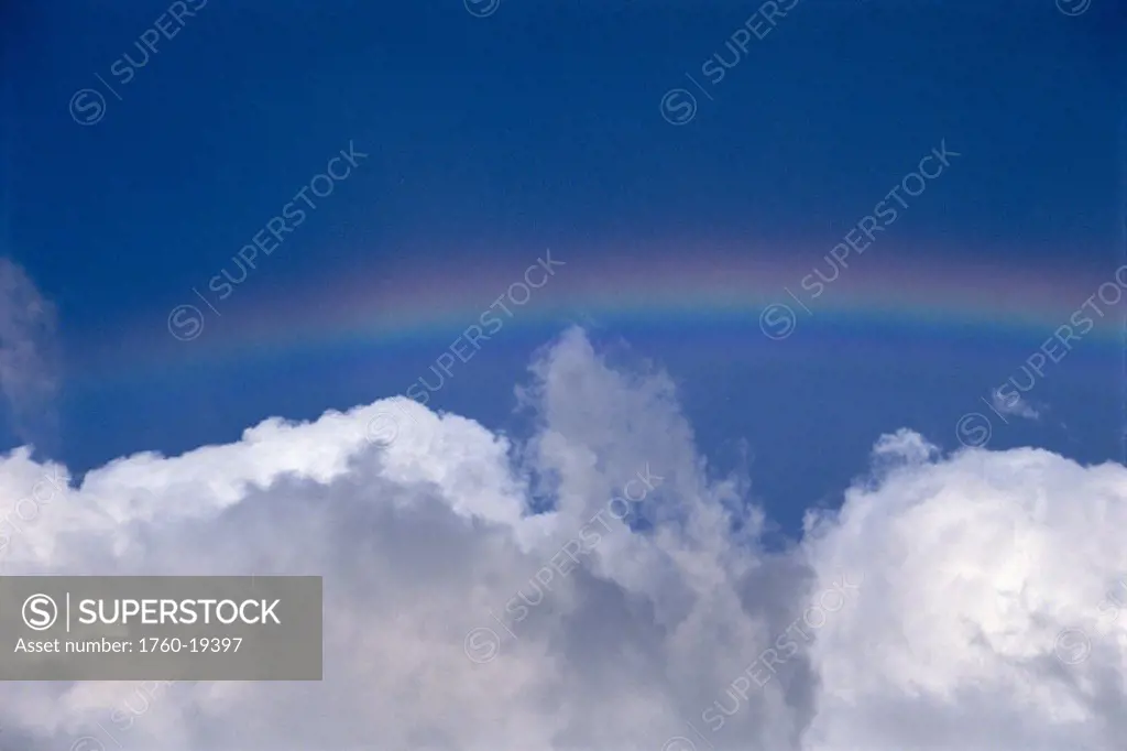Rainbow over puffy white clouds in blue sky