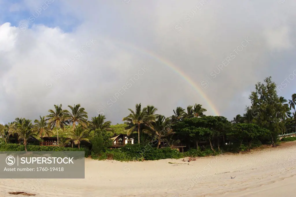 Hawaii, Oahu, North Shore, rainbow arching over vegetation and sandy beach.