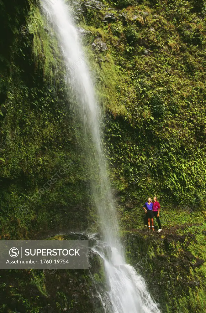 Hawaii, Big Island, North Kohala, Kapoloa Falls, couple on trail look up at cascading waterfall