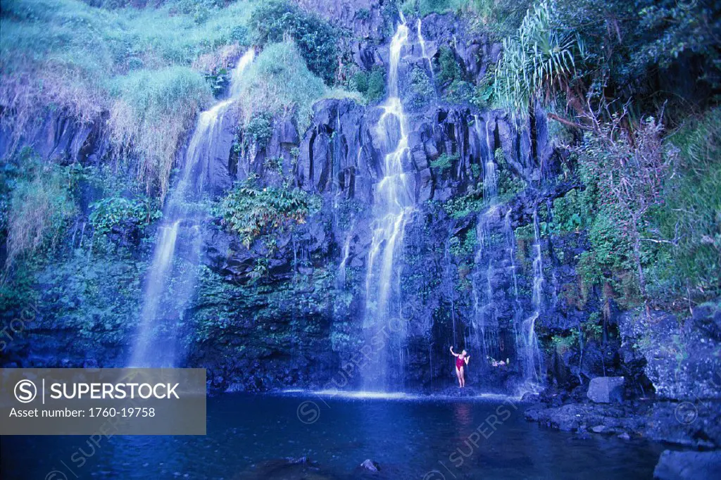 Hawaii Maui Hana woman in red bathingsuit stands beneath cascading falls, blue pools