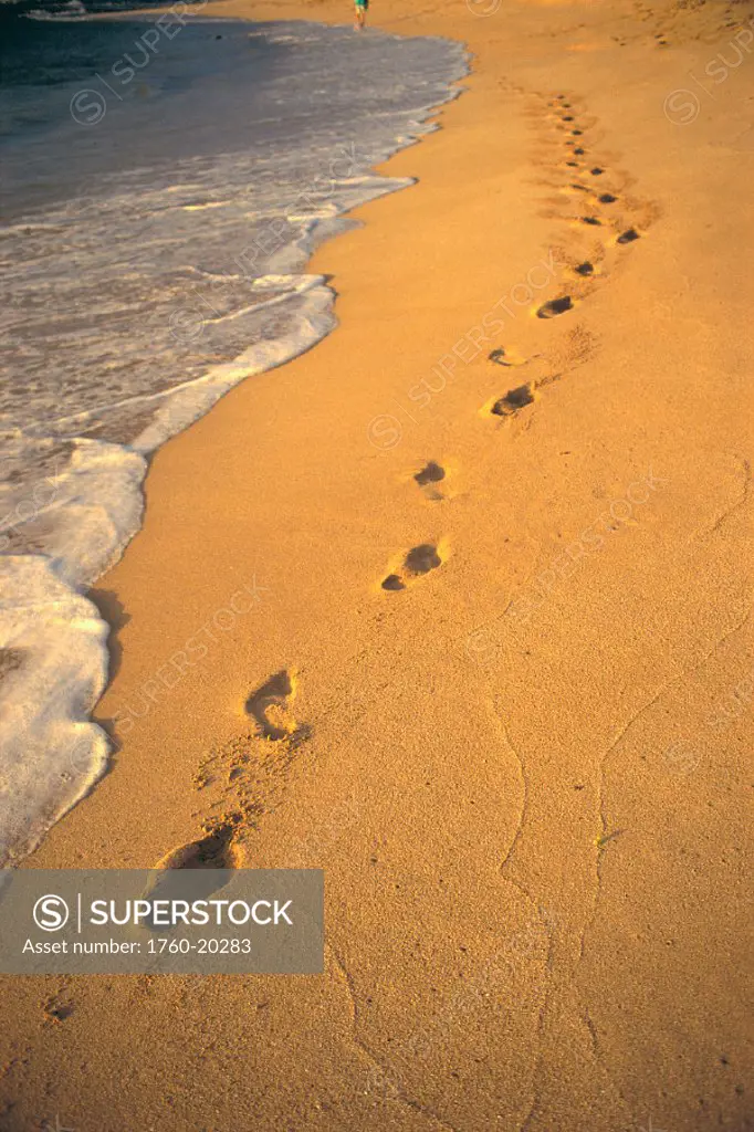 Footprints along shoreline waters in golden sand