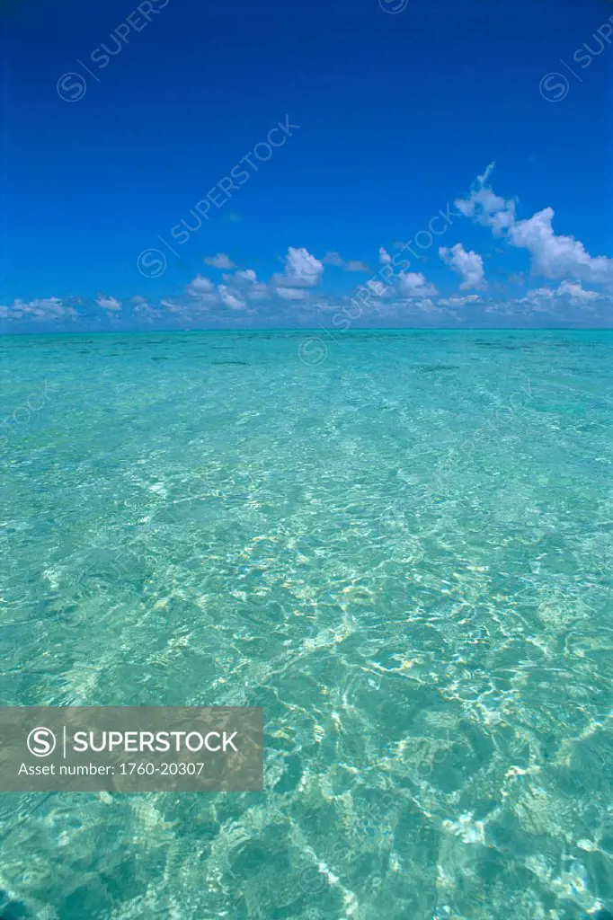 Clear turquoise ocean water, blue sky, white clouds, sunlight reflections