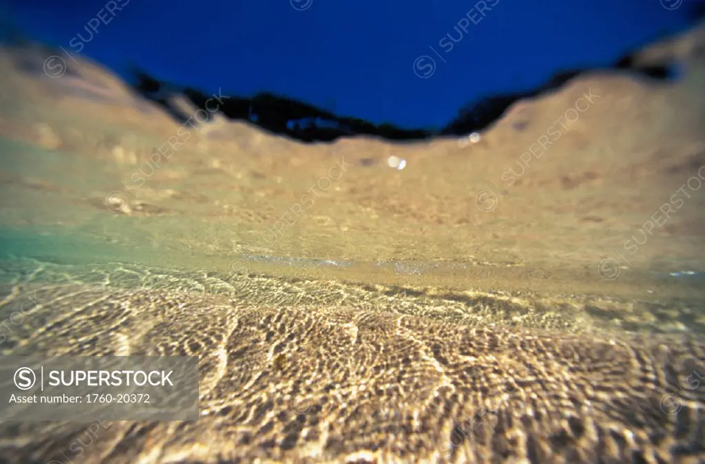 Underwater reflections along sandy bottom, at surface blue sky visible
