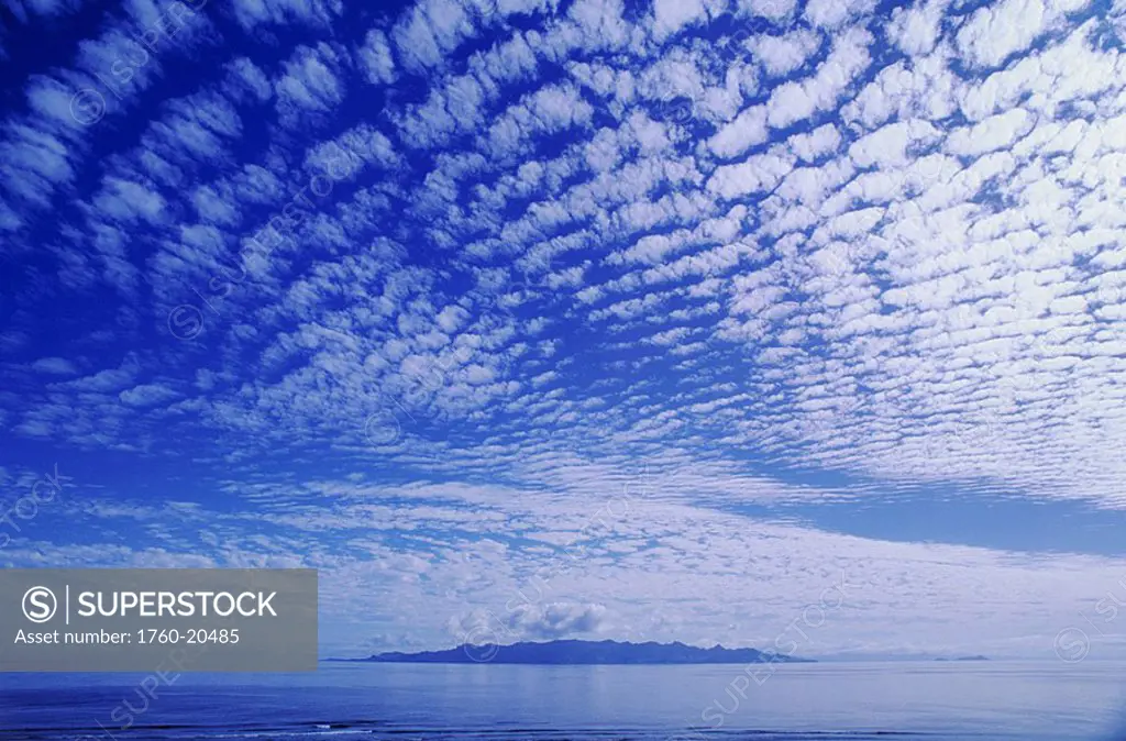 Cotton-like clouds in blue sky over smooth ocean water, Island in distance