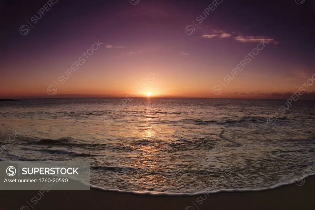 Hawaii, Oahu, North Shore, water lapping onto shore of a beautiful sandy beach at sunset.