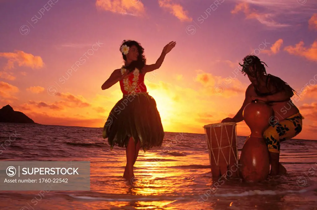 Hula dancer performing with drummer on beach at sunrise in background Hawaii