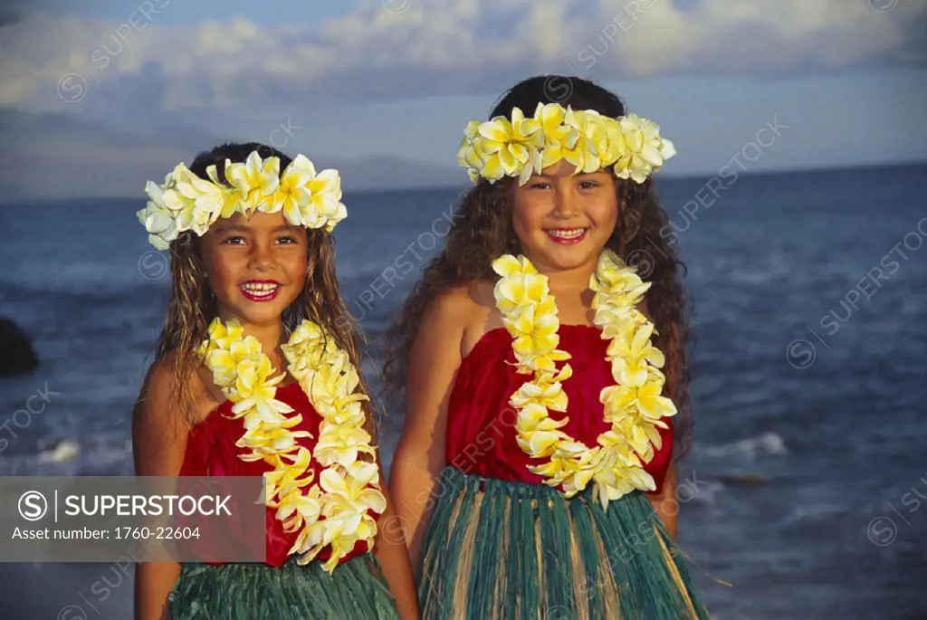 Two young girls with plumeria leis in hula dress smiling on beach