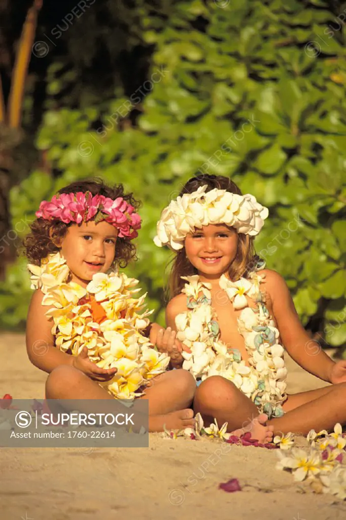 Two keiki on beach with flowers and lei, smiling