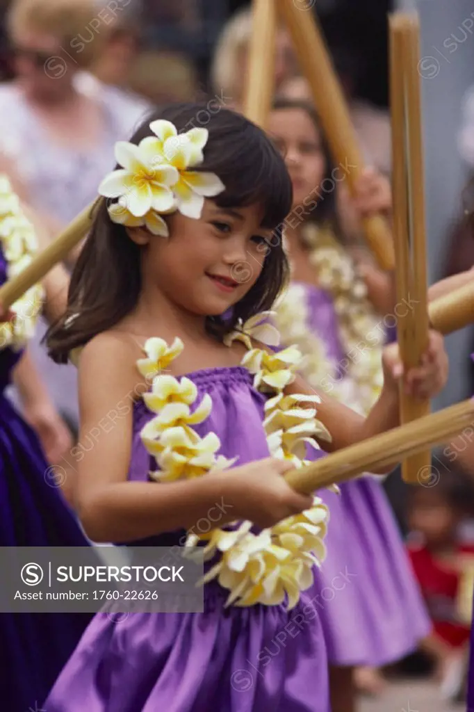 Young keiki girl playing with bamboo sticks with plumeria lei warm smile.