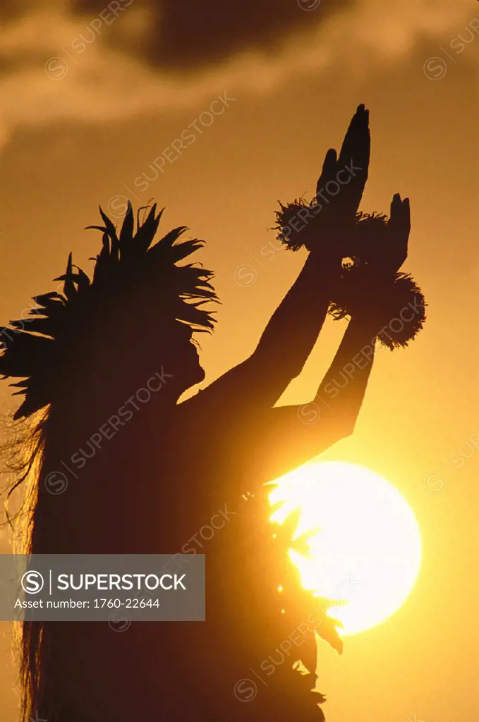 Closeup of woman silhouetted at sunset w/ sunball, pale orange sky, Kahiko hula