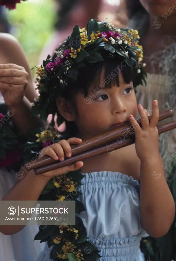 Close-up of little Asian hula girl with floral lei and haku, holding kala´au (sticks)