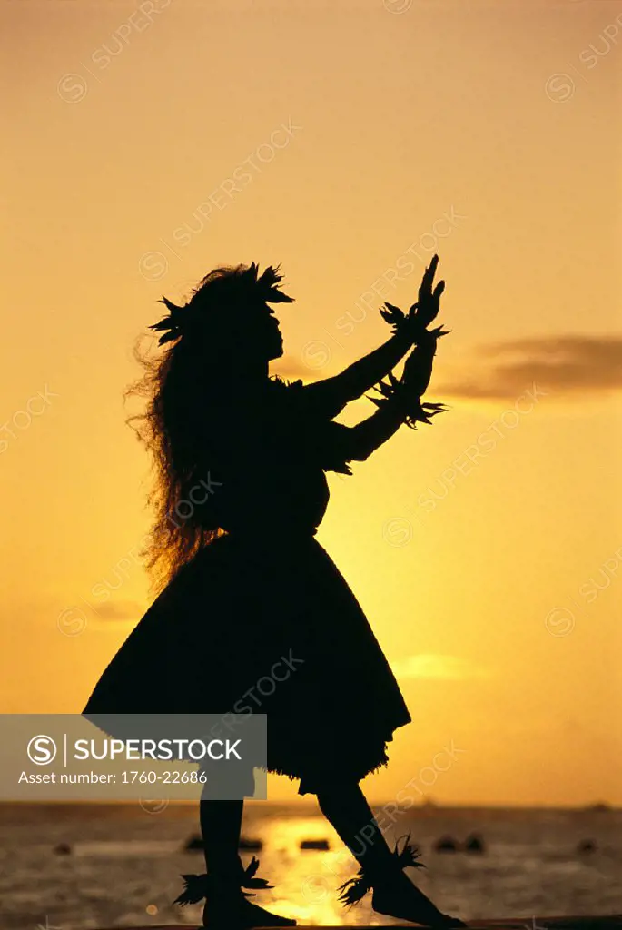 Hawaii, female hula dancer at beach, silhouetted by golden sunset, reflections on ocean