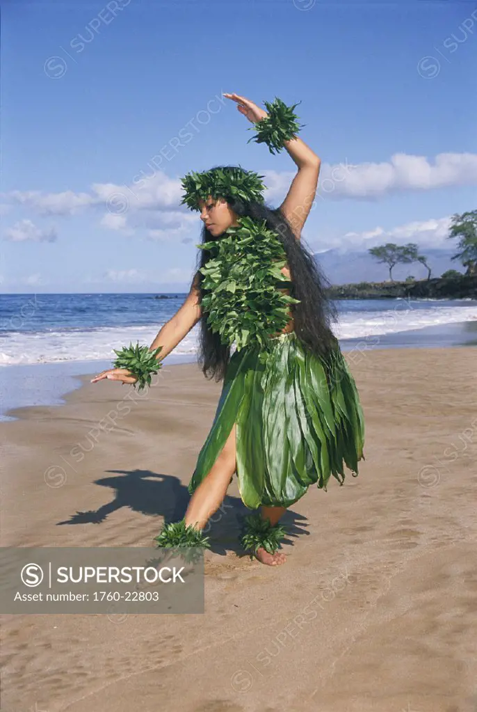 Hula dancer in ti-leaf skirt in a dancing pose on the beach