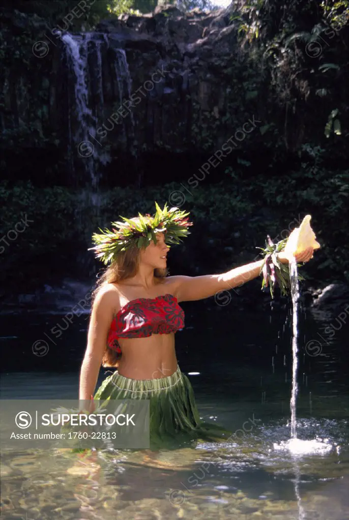 Hula dancer in water, holding shell, waterfall in background