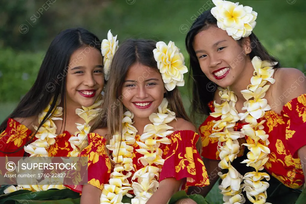 Three girls in colorful hula outfits, matching w/ plumeria lei & flowers, smiling Hawaii Maui
