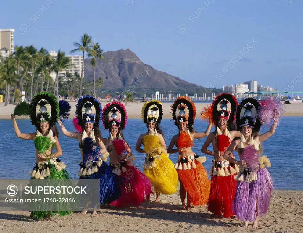 Seven smiling Tahitian dancers in colorful outfits, Diamond Head & Waikiki bkgd