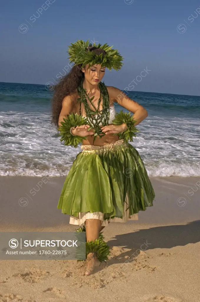 Hula dancer in ti-leaf skirt, haku, lei, in a dancing pose on the beach