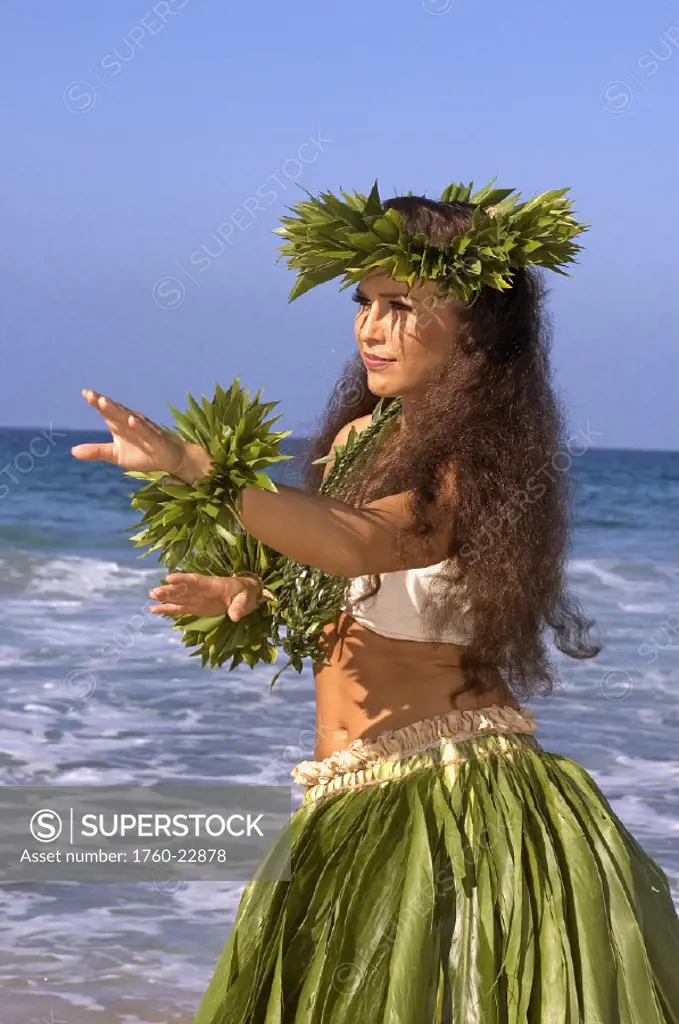 Hula dancer in ti-leaf skirt, haku, lei, in a dancing pose on the beach