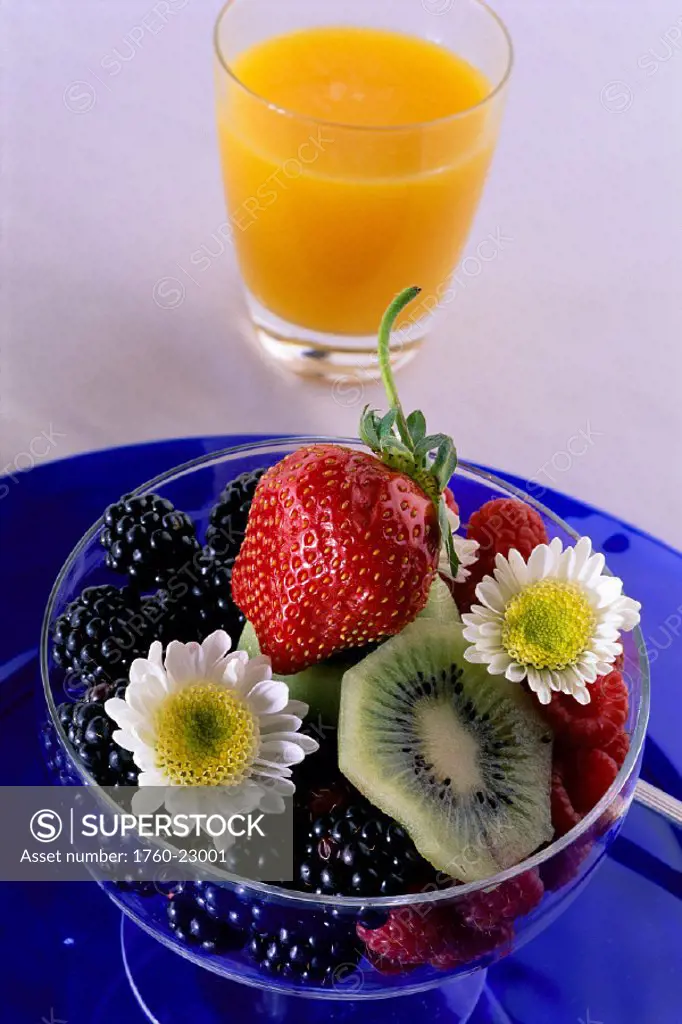 Closeup of a glass of orange juice with a bowl of fresh berries on blue dish C1175